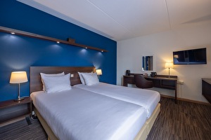 Comfort kamer in Amrâth Hotel Media Park Hilversum met twee eenpersoonsbedden met een blauwe muur, een bureau, een stoel, een tv en een raam met veel daglicht