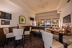 Hotelbar in Amrâth Hotel Media Park Hilversum, met witte muren, witte leren stoelen, houten tafels en een  kroonluchter als decoratie.