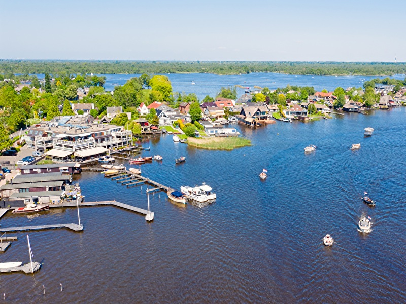 Luchtfoto van de Loosdrechtse Plassen met boten op het water en huizen langs de oever op een zonnige dag.
