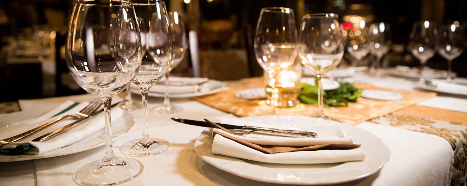 Ein schön gedeckter Tisch mit Gläsern und weißen Tellern, bereit für ein köstliches Abendessen.