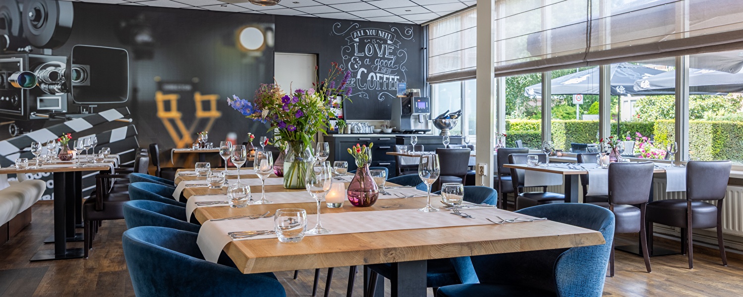 Modern restaurant van Amrâth Hotel Media Park Hilversum met filmthema en grote ramen, sfeervol ingericht met verse bloemen, stijlvol servies en uitzicht op het terras.