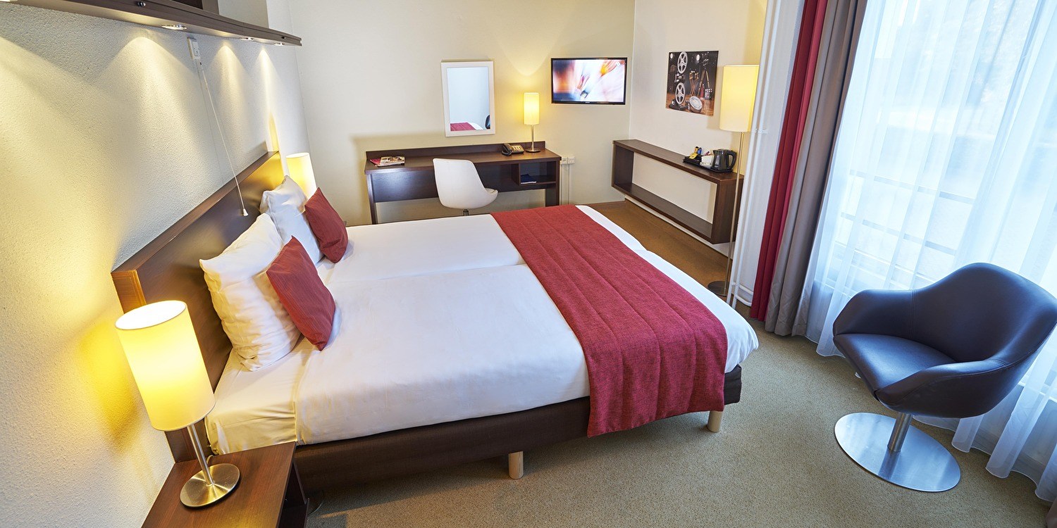 Hotelkamer in het Amrâth Hotel Media Park Hilversum, met twee bedden, bureau, tv en zithoek bij het raam.