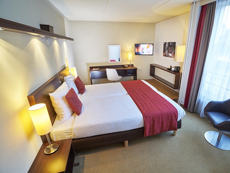 Hotelkamer in het Amrâth Hotel Media Park Hilversum, met twee bedden, bureau, tv en zithoek bij het raam.