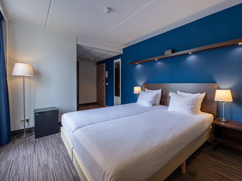 Hotelkamer in het Amrâth Hotel Media Park Hilversum, met twee bedden, bureau, tv en zithoek bij het raam.