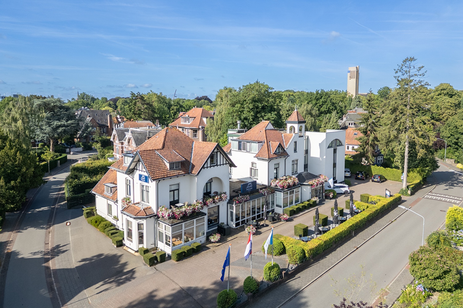 Amrâth Hotel Media Park in Hilversum, lichte gevel met kleurrijke bloemen en buitenzitplaatsen.