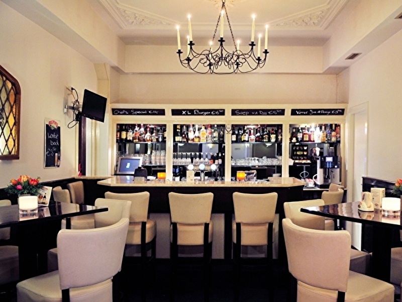 Interieur van de bar in het Amrâth Hotel Media Park Hilversum, met een lange toog, zitgedeelte en kroonluchter.