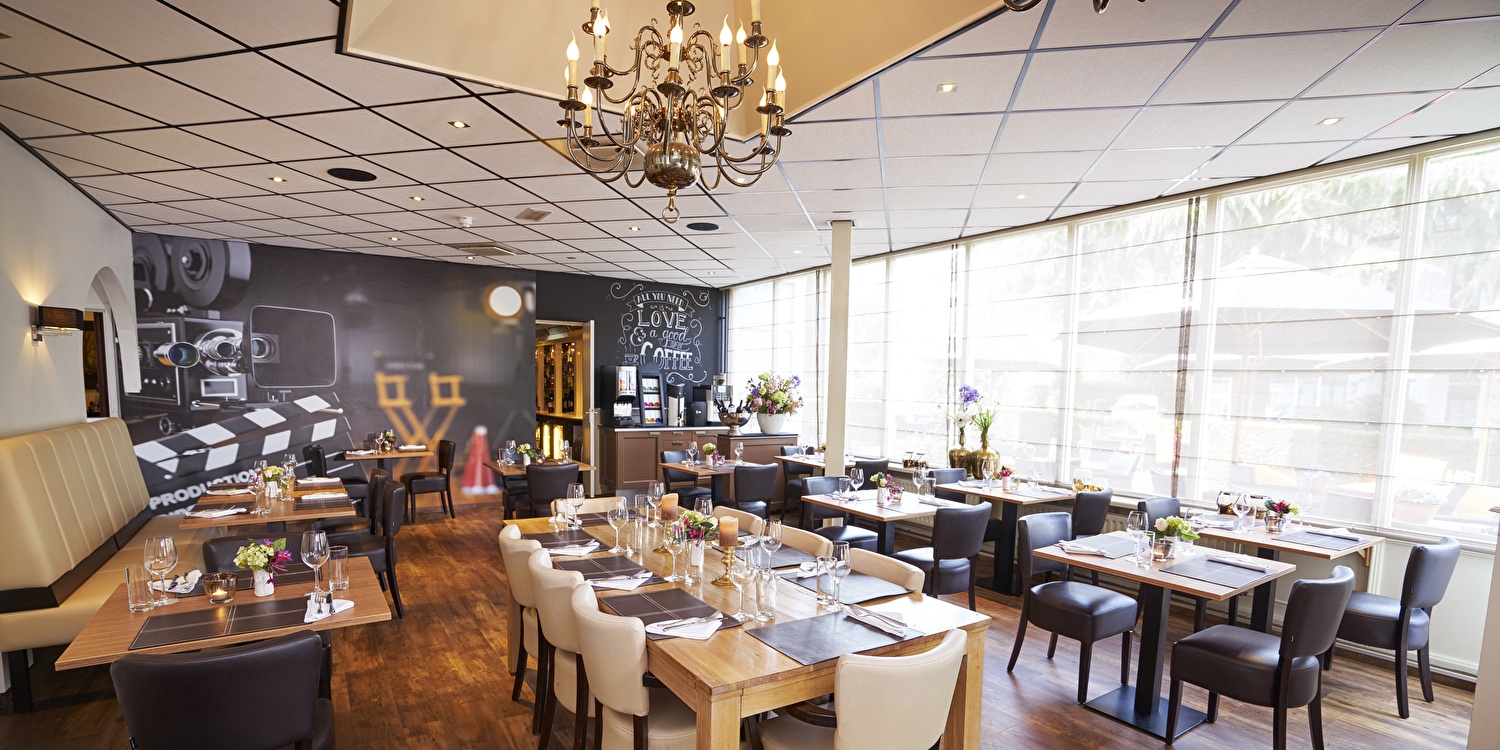 Restaurant in Amrâth Hotel Media Park Hilversum met meerdere tafels en stoelen die zijn opgedekt.