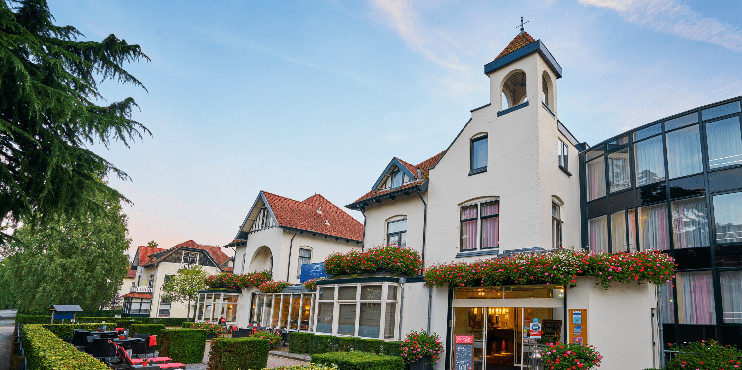 Amrâth Hotel Media Park in Hilversum, lichte gevel met kleurrijke bloemen en buitenzitplaatsen.