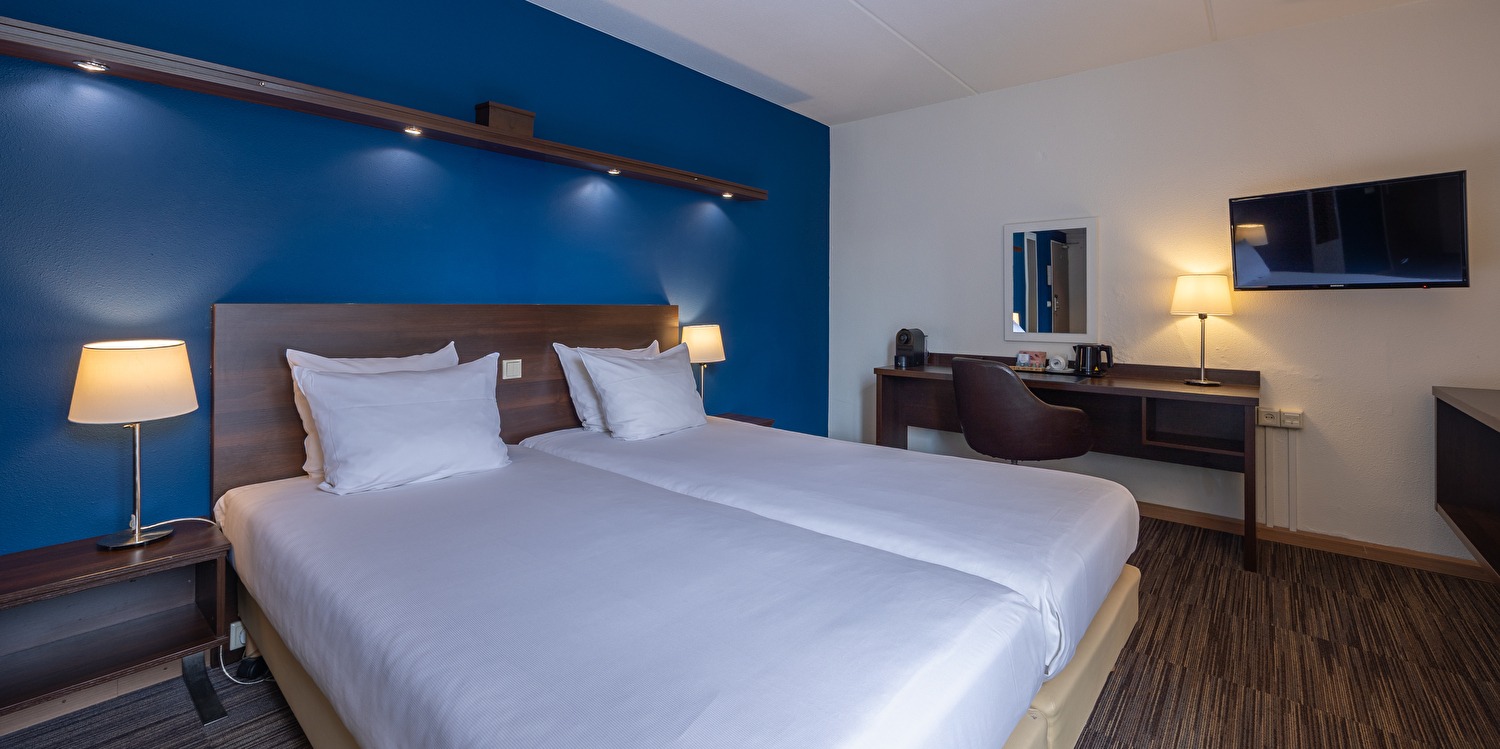 Comfort kamer in Amrâth Hotel Media Park Hilversum met twee eenpersoonsbedden met een bureau, een stoel, een tv en een raam met veel daglicht