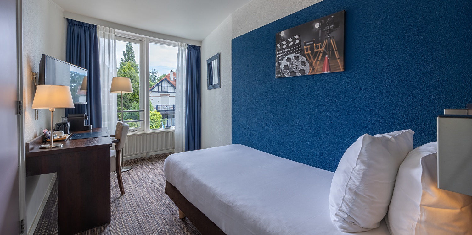 Single kamer in Amrâth Hotel Media Park Hilversum met een eenpersoonsbed met een bureau, een stoel, een tv en een raam met veel daglicht