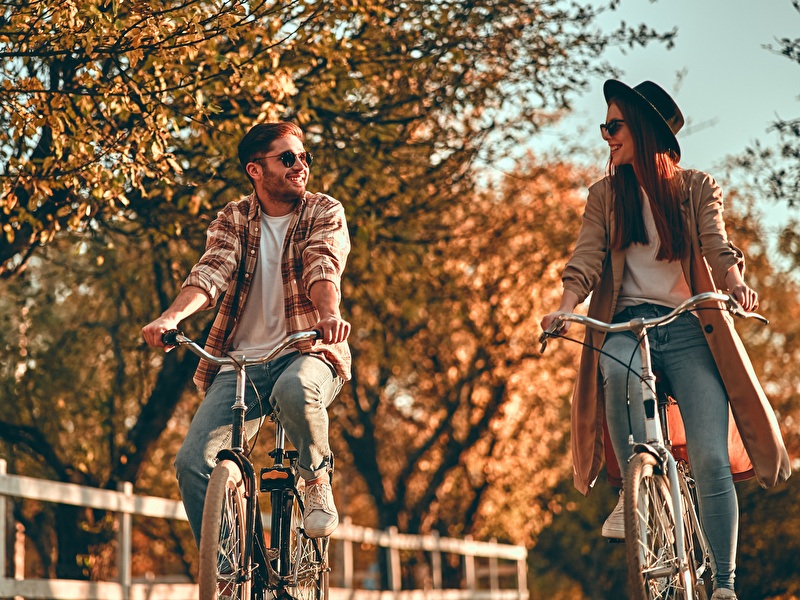 Man und Frau fahren lachend nebeneinander auf einem sonnigen Herbsttag Fahrrad.