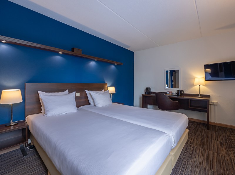 Comfort room in Amrâth Hotel Media Park Hilversum with a double bed with a blue wall, a black chair, and a TV on the wall
