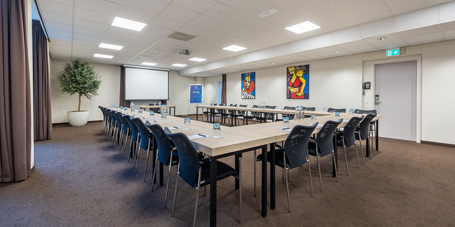 Versammlungsraum des Amrâth Hotel Media Park Hilversum mit U-Anordnung, modernen audiovisuellen Mitteln, Projektionsleinwand und bequemen Stühlen.